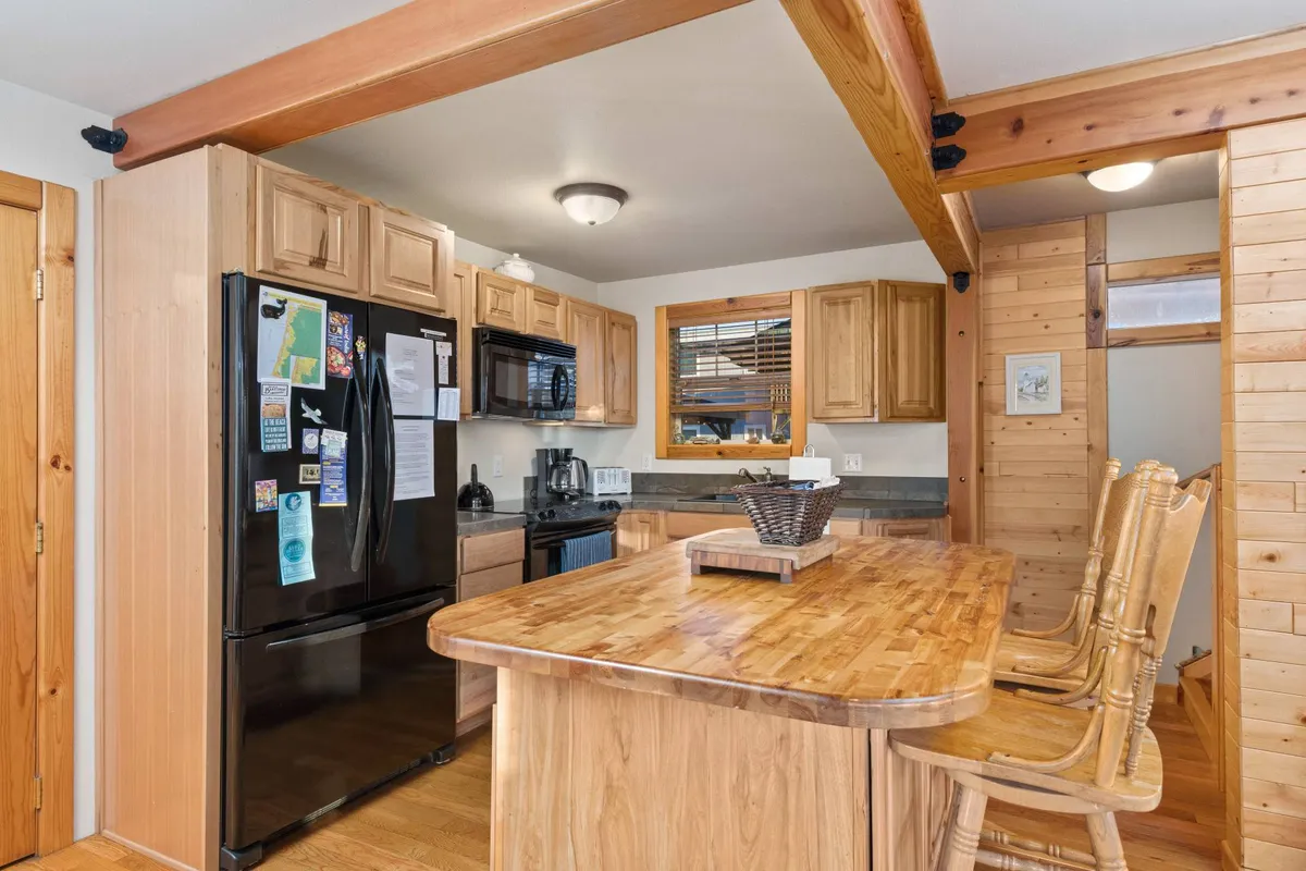 A cozy kitchen scene featuring a central kitchen island, black refrigerator, wooden cabinets, and bar stools, inviting people to gather for cooking, casual dining, and conversation.