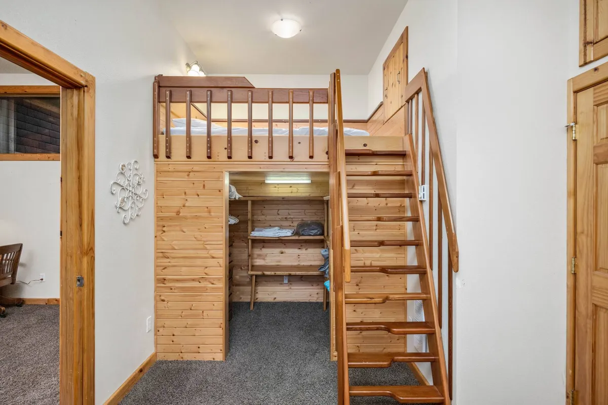 This image features a lofted bed accessed by a wooden staircase, with wooden storage areas beneath. The cozy setup suggests a playful and inviting sleeping or hangout area perfect for kids or adventurous sleepers, and the wood tones create a warm, family-friendly ambiance.