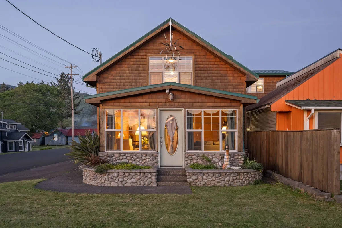 A welcoming exterior view of Cedar Lodge, showcasing its wooden facade, large windows that let in natural light, a stone pathway leading to the entrance, and a distinctive decorative door. The surrounding greenery hints at a peaceful and inviting setting.