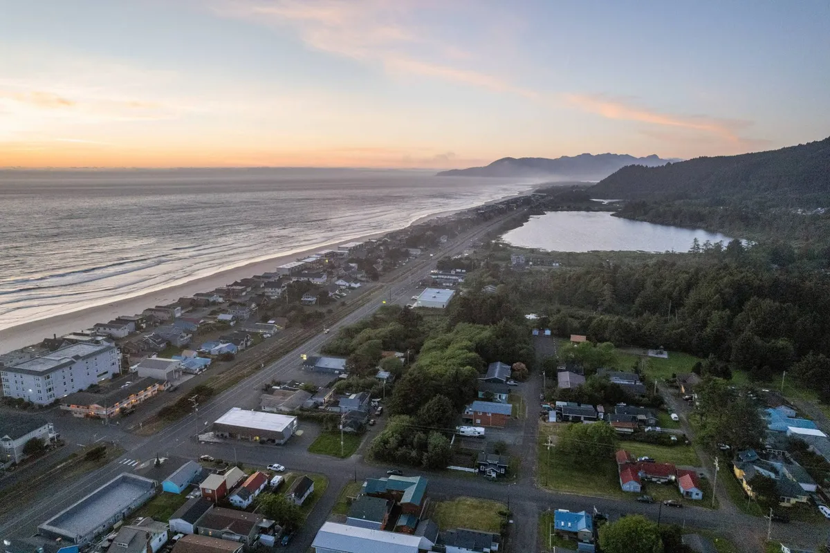 A sweeping coastal view with the ocean, sunset, mountains, and glimpses of the nearby town and lake. The tranquil scene captures the beauty and wide-open spaces of Rockaway Beach—ideal for long walks, outdoor adventures, and quality time with your canine companion.