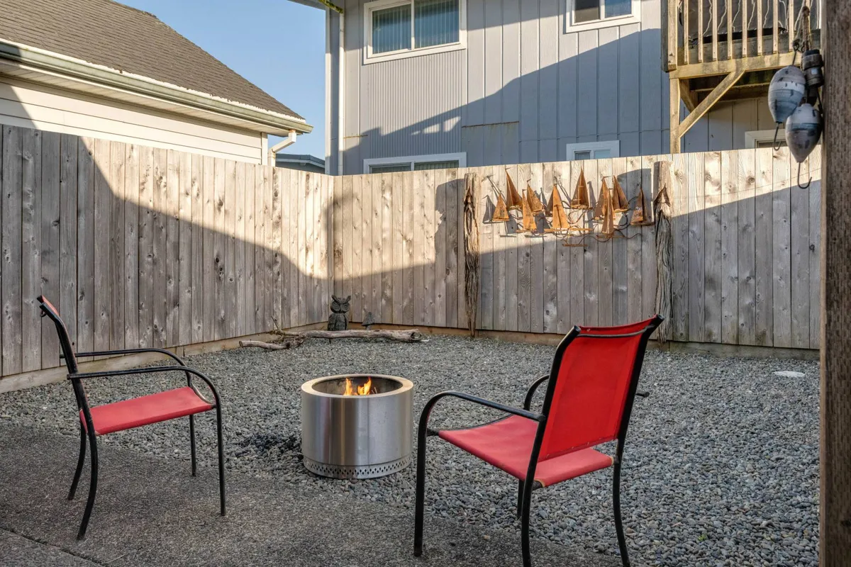 A fenced outdoor area focused on a fire pit encircled by red chairs and bordered by a wooden fence. The setup, simple and welcoming, suggests a safe, enclosed space ideal for pets and relaxed socializing under the stars.