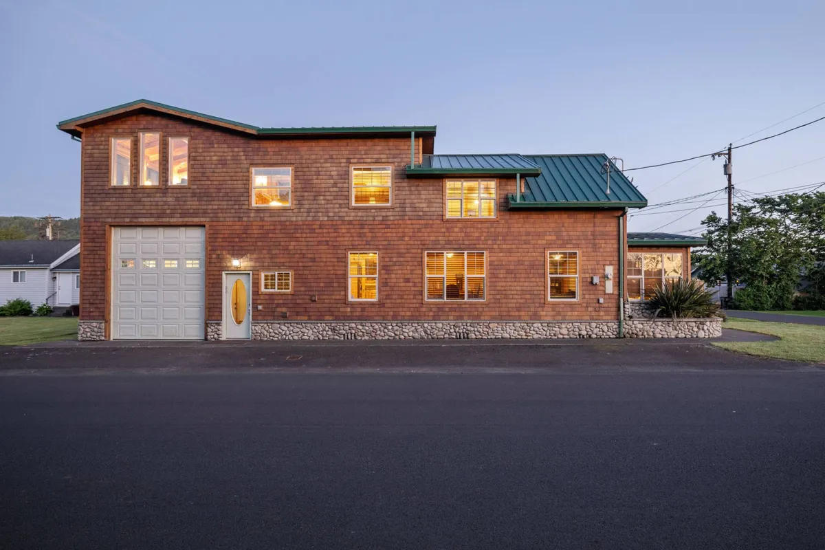 A welcoming view of the Cedar Lodge exterior, featuring wooden siding, a green metal roof, brightly lit windows, and a front door leading to a spacious yard. The scene suggests ample outdoor space ideal for families and pets, with the inviting look of the home setting the stage for relaxation and play.