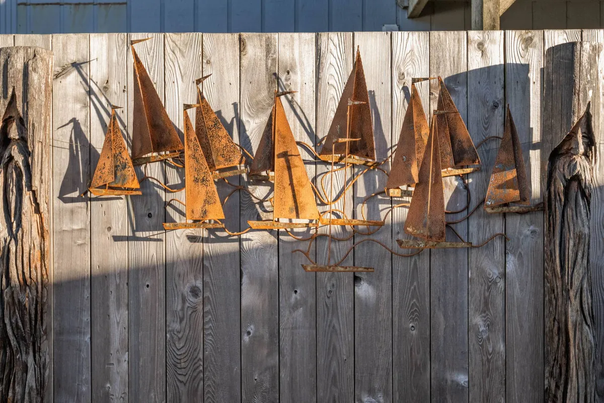 An exterior scene featuring rusted sailboat sculptures artfully arranged beside a weathered wooden fence, evoking the creative, coastal spirit of the area. The image hints at a playful, pet-friendly outdoor space with unique artistic touches.